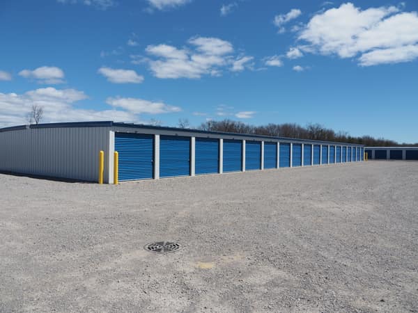 Building D at Perimeter Road Self Storage: a long row of blue drive-up unit doors under a clear sky